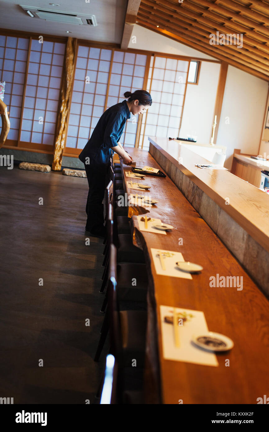 Serveuse debout à un comptoir dans un restaurant de sushi japonais, la préparation placez les paramètres. Banque D'Images