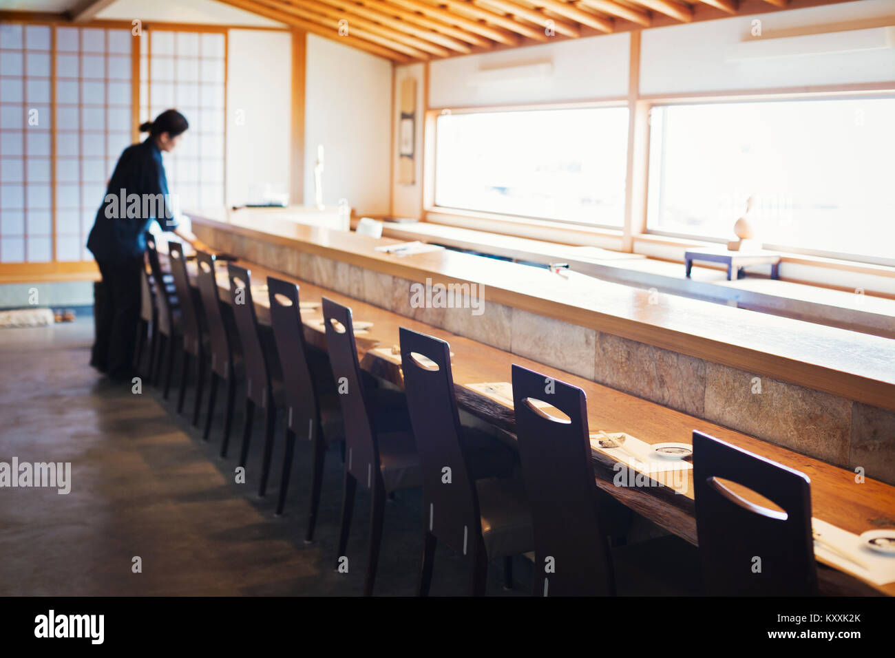 Serveuse debout à un comptoir dans un restaurant de sushi japonais, la préparation placez les paramètres. Banque D'Images