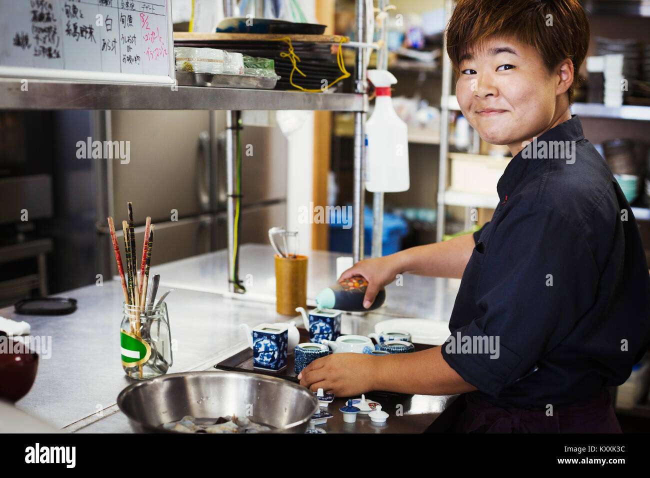 Serveuse travaillant dans la cuisine d'un restaurant de sushi japonais, smiling at camera. Banque D'Images