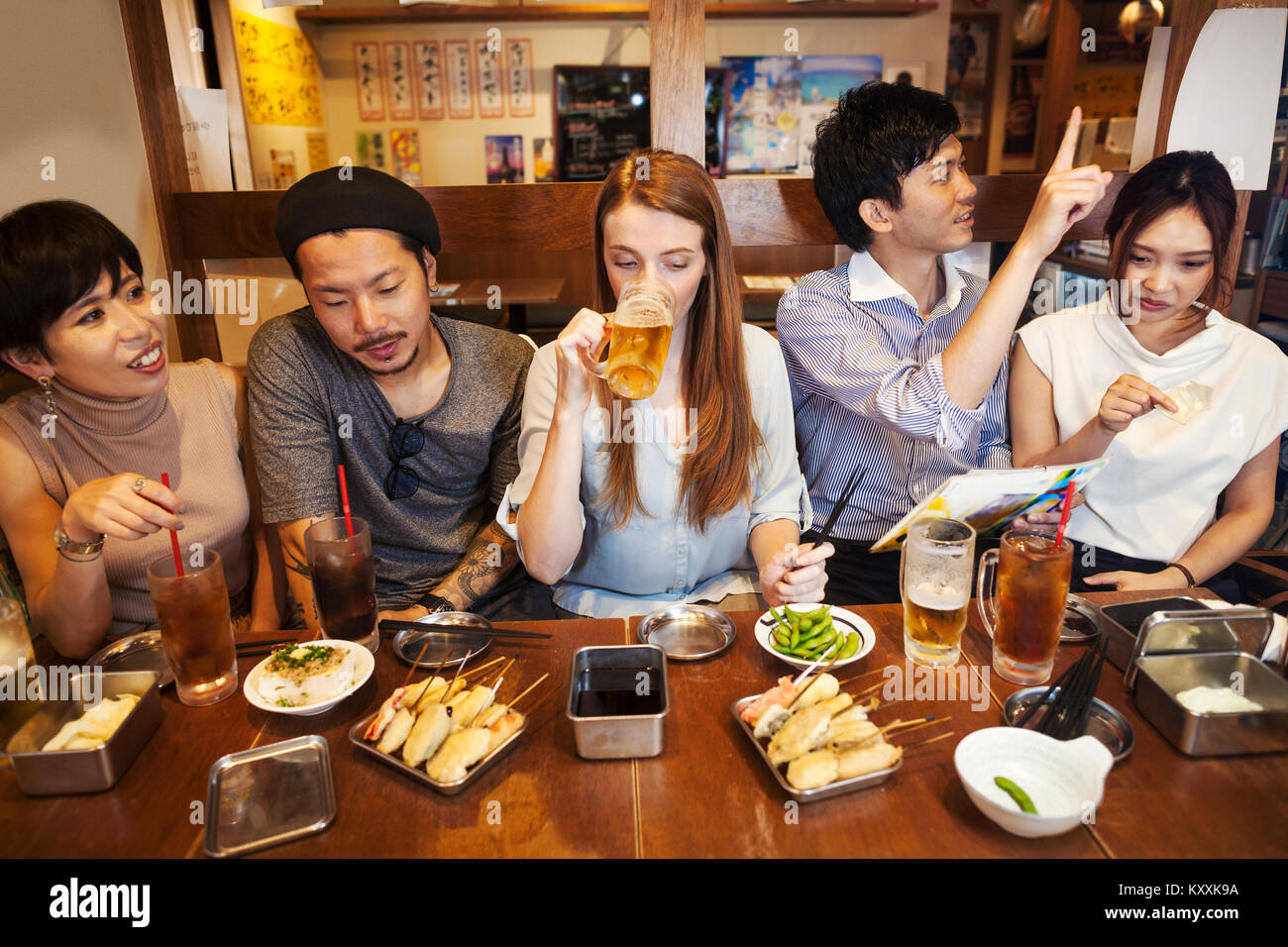 Cinq personnes assis à côté par sidy une table dans un restaurant, manger et boire de la bière. Banque D'Images