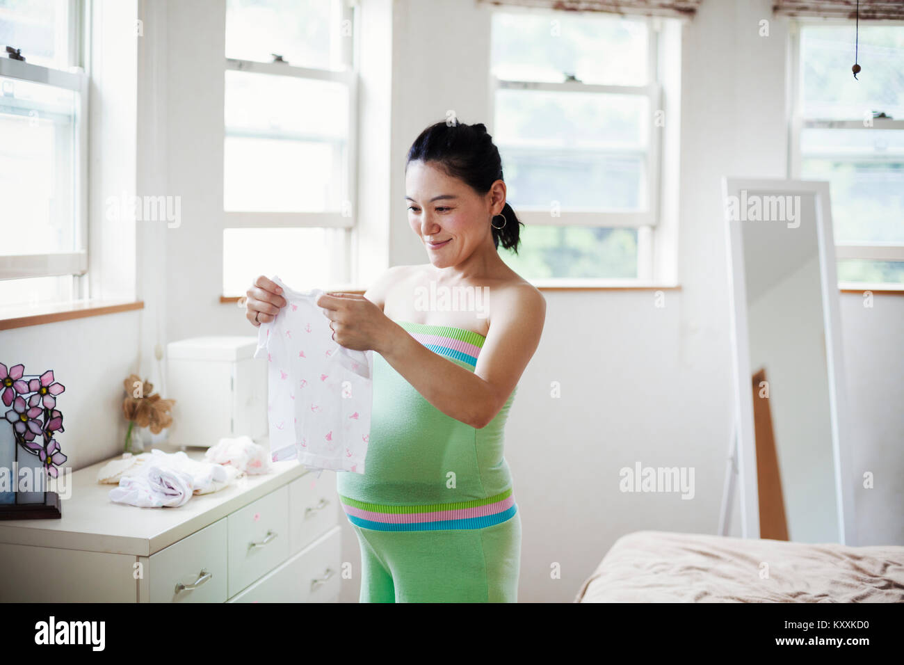 Une femme enceinte dans une pépinière de bébé prix, pliage de vêtements de bébé. Banque D'Images