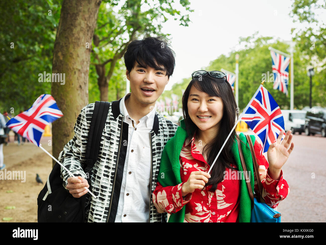 Sourit l'homme et la femme aux cheveux noirs se tenant debout sur le côté d'une route urbaine bordée d'exploitation, de petits drapeaux Union Jack, looking at camera. Banque D'Images