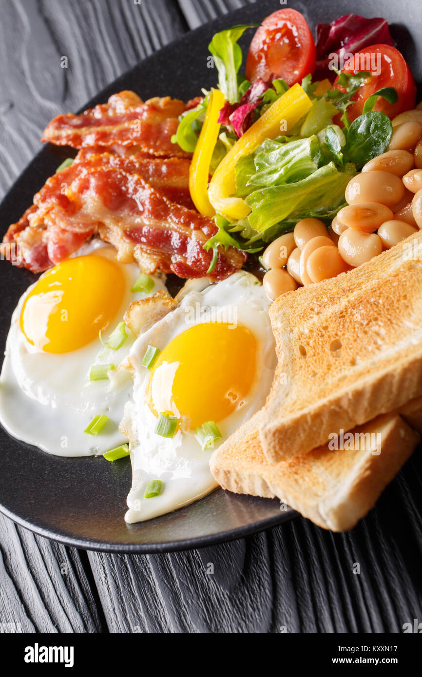 Petit déjeuner copieux oeufs au plat avec du bacon, des haricots, du pain grillé et salade de