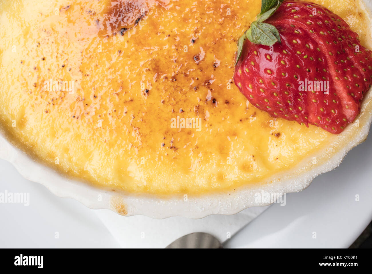 Crème dessert sucré et crémeux faite d'oeufs, le lait et le sucre surmonté d'une fraise en tranches dans une assiette blanche Banque D'Images