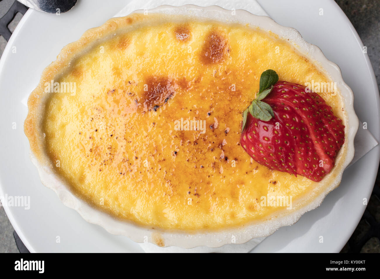 Crème dessert sucré et crémeux faite d'oeufs, le lait et le sucre surmonté d'une fraise en tranches dans une assiette blanche Banque D'Images