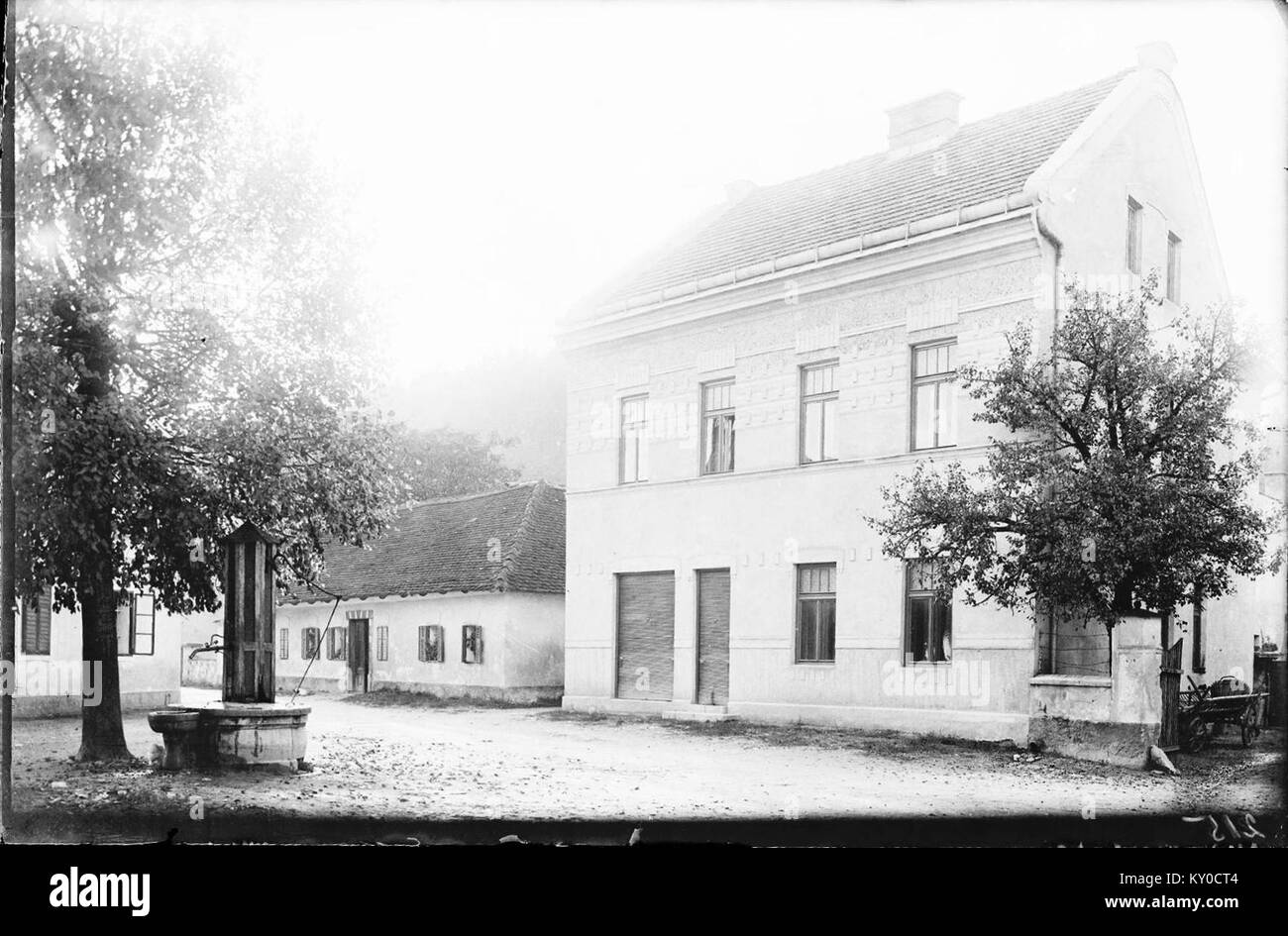 Cette image de 1913 montre une maison et un puits à Mengeš, Slovénie, reflétant l'architecture résidentielle traditionnelle et les méthodes d'accès à l'eau. Banque D'Images