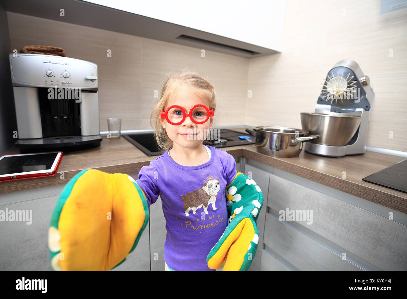 Funny Girl en grande cuisine mitaines. Smiling blonde petite fille s'amuse à la maison. Banque D'Images