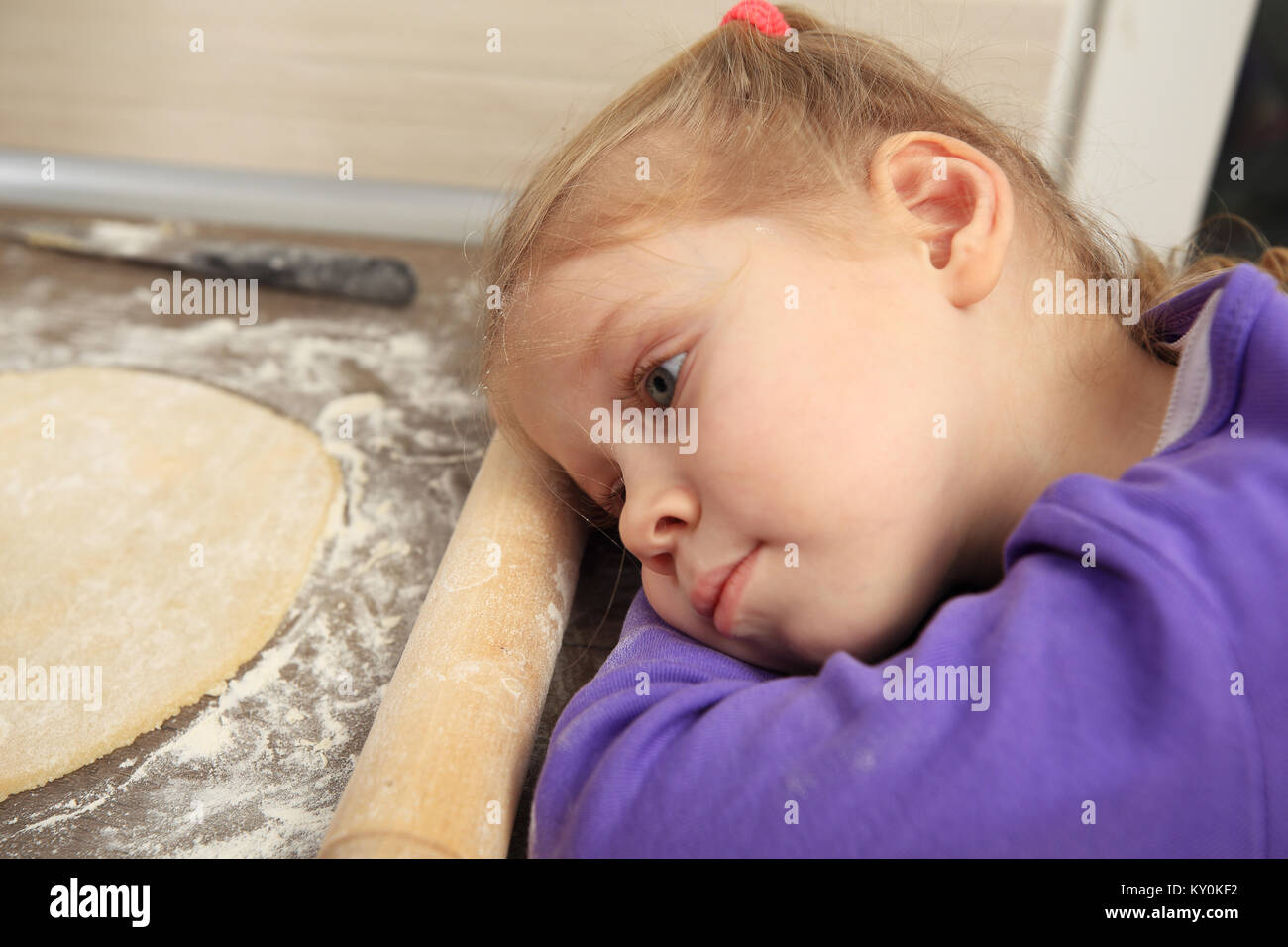 Portrait de l'enfant fatigué dans la cuisine. Petite fille blonde dormir près de la pâte. Banque D'Images