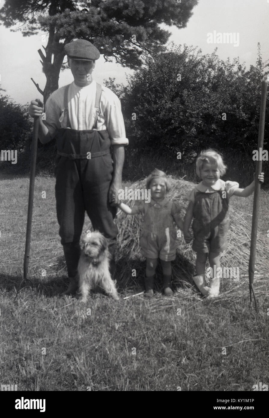 Annees 1950 Historique Deux Jeunes Filles L Une Tenant Un Long Traite En Bois Fourche Se Tenir Fierement A Cote Du Pere Un Fermier A L Exterieur Dans Un Champ Fauche Recemment England Uk
