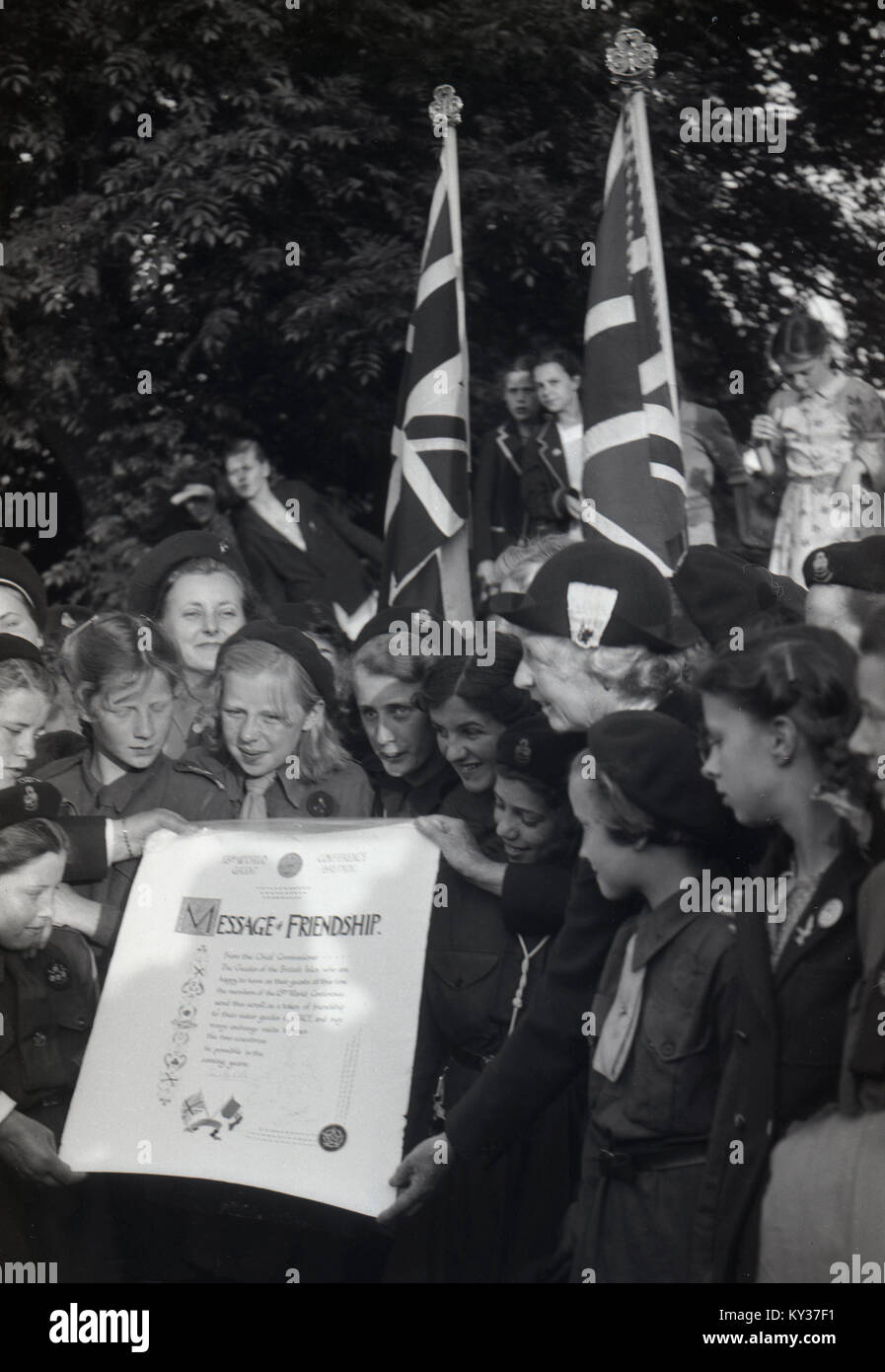 1950, tableau historique d'un groupe de jeunes guides avec l'Union jack drapeaux et brandissant une 'message d'amitié' à la 13e Conférence mondiale tenue à la Women's College, seul St Hugh's, l'Université d'Oxford, Angleterre, Royaume-Uni. Banque D'Images