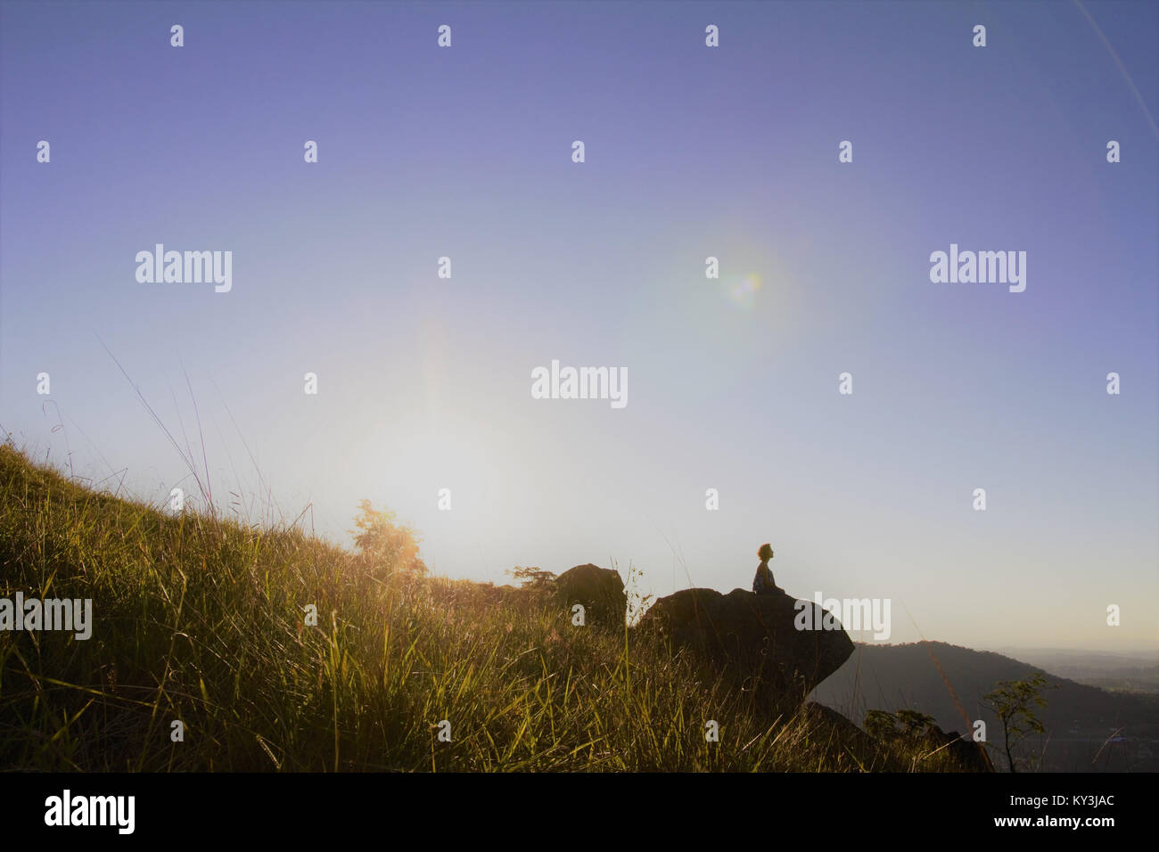 Jeune femme médite sur le haut de la colline, pendant le coucher du soleil. Banque D'Images