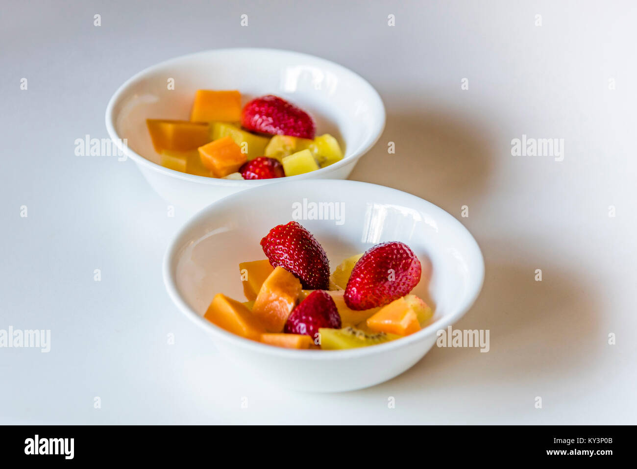 Salade de fruits frais colorés en blanc bols, vue de côté. Deux plats blanc de coupe de fruits mélangés en santé, fond blanc, libre. Banque D'Images