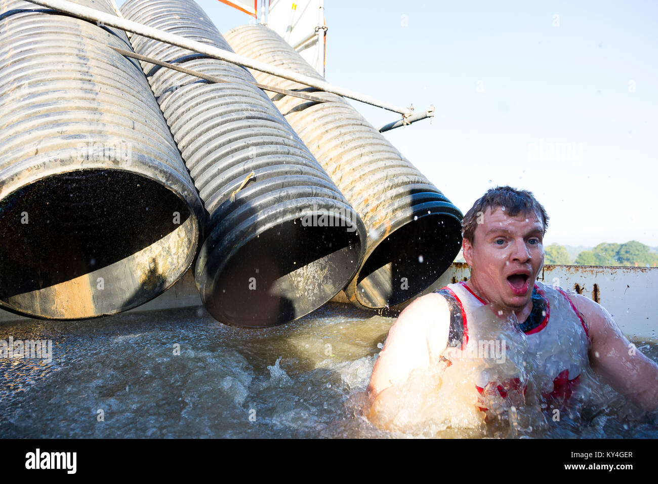 Sussex, UK. Un jeune homme tire un visage choqué alors qu'il émerge d'un bassin d'eau glacée pendant une dure Mudder course à obstacles. Banque D'Images
