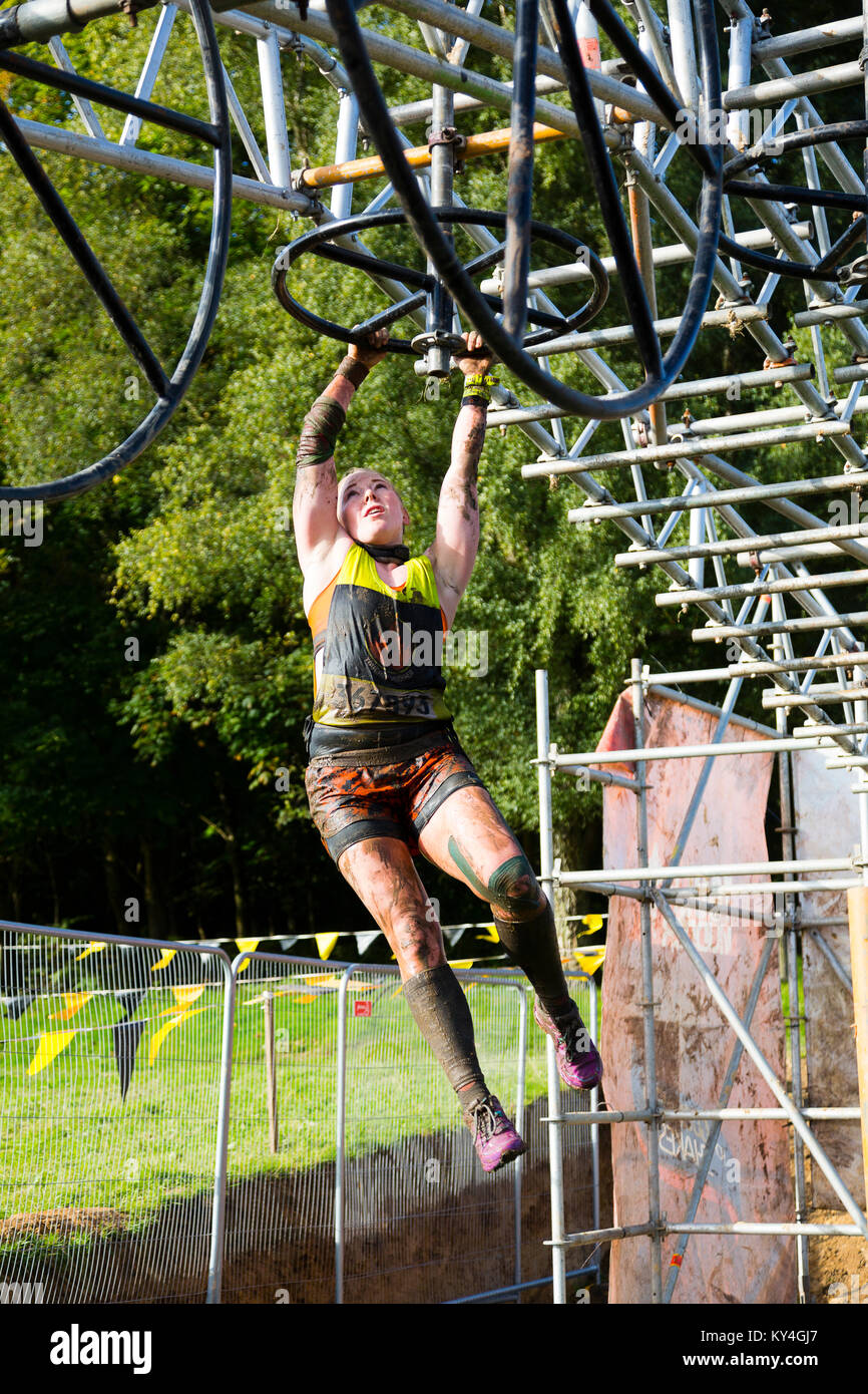 Sussex, UK. Une femme comme elle balançoires concurrent se concentre sur son chemin d'un bassin d'eau à l'Hangin' Tough Tough Mudder obstacle pendant un événement. Banque D'Images