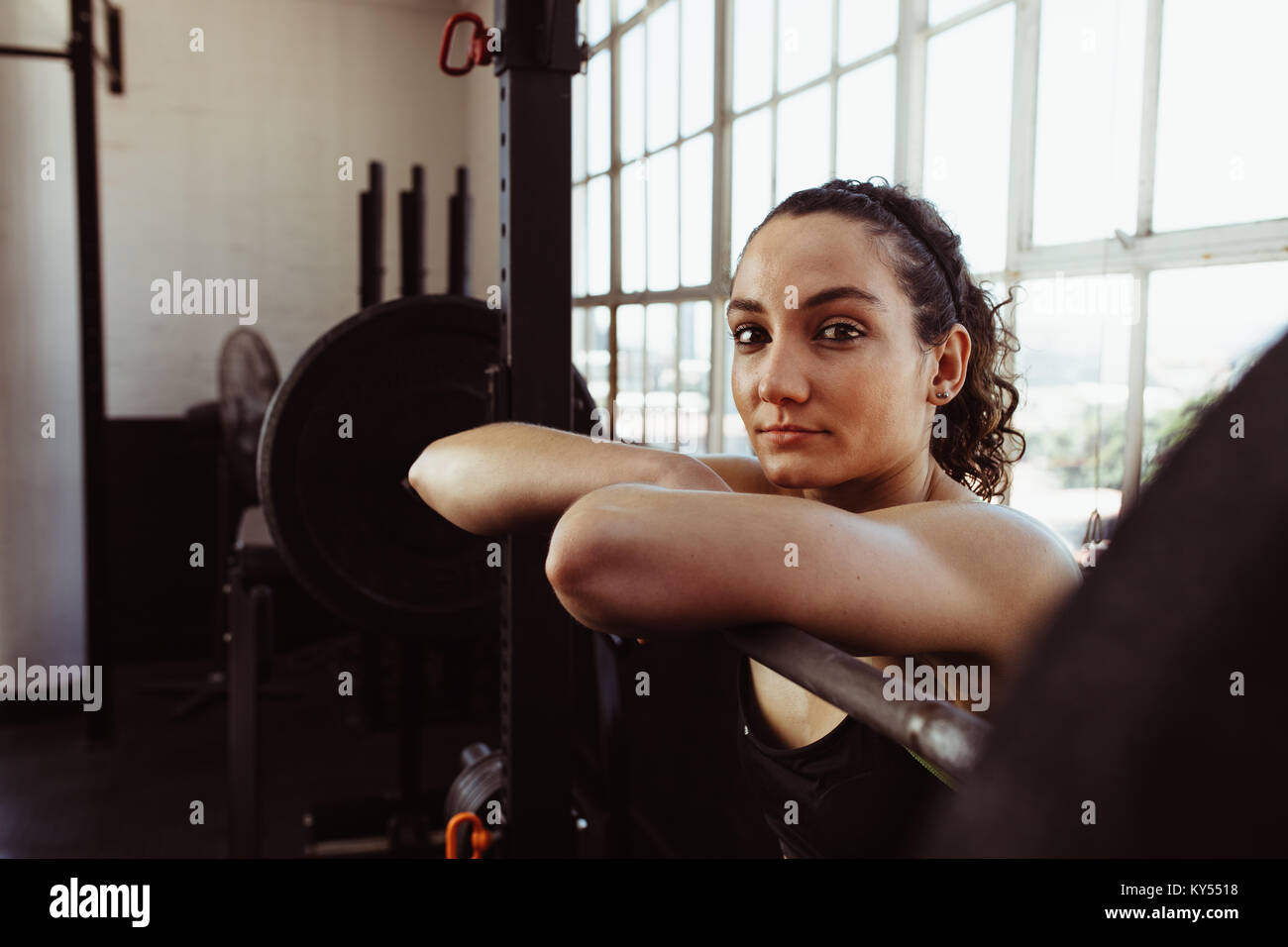 Young woman leaning over barbell après une formation dans une salle de sport. Prise femelle reste après l'entraînement physique dans un club de santé. Banque D'Images
