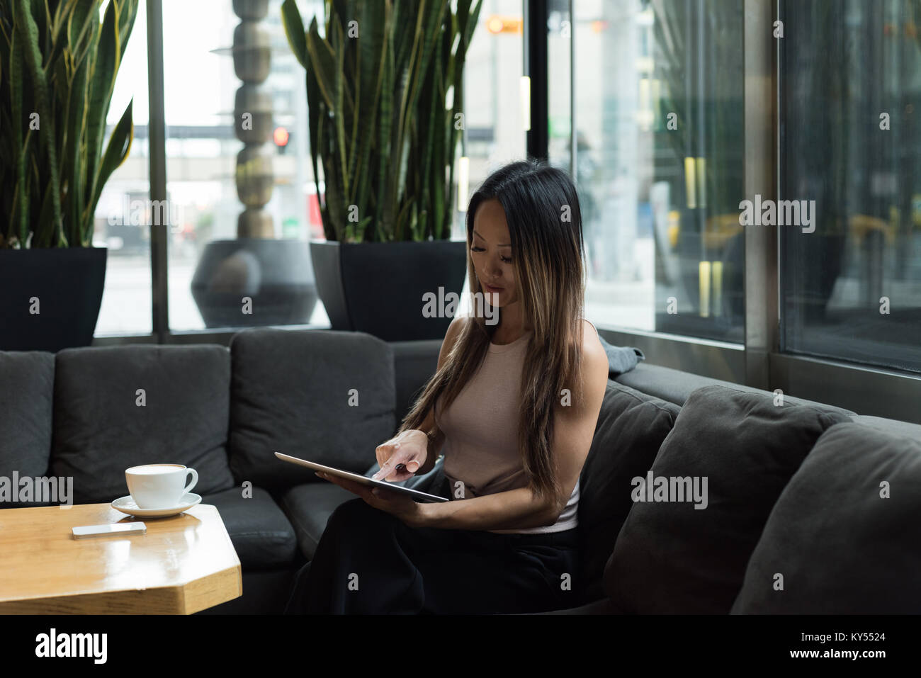 Businesswoman sitting on sofa working on her tablet Banque D'Images