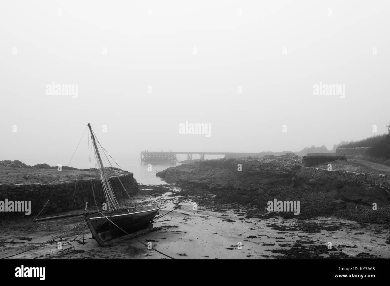 Un voilier couché sur le côté comme la marée basse sur une plage misty en Ecosse. Une jetée peut être vu dans la distance qu'un gel misty mist entre en jeu. Banque D'Images