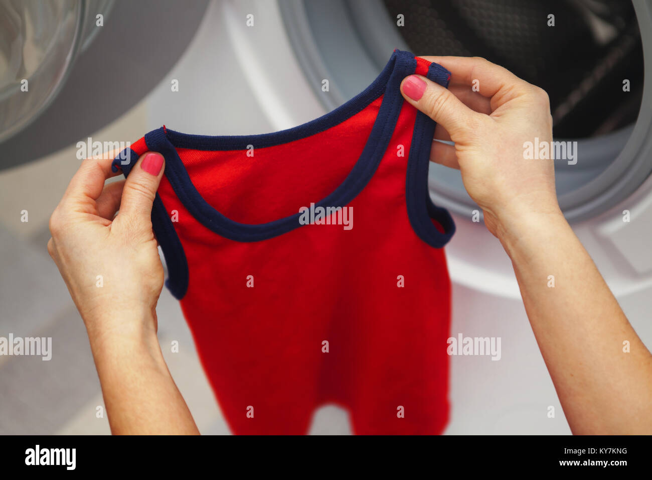 L'enfant rouge T-shirt dans les mains d'une femme qui inspecte elle avant le lavage Banque D'Images