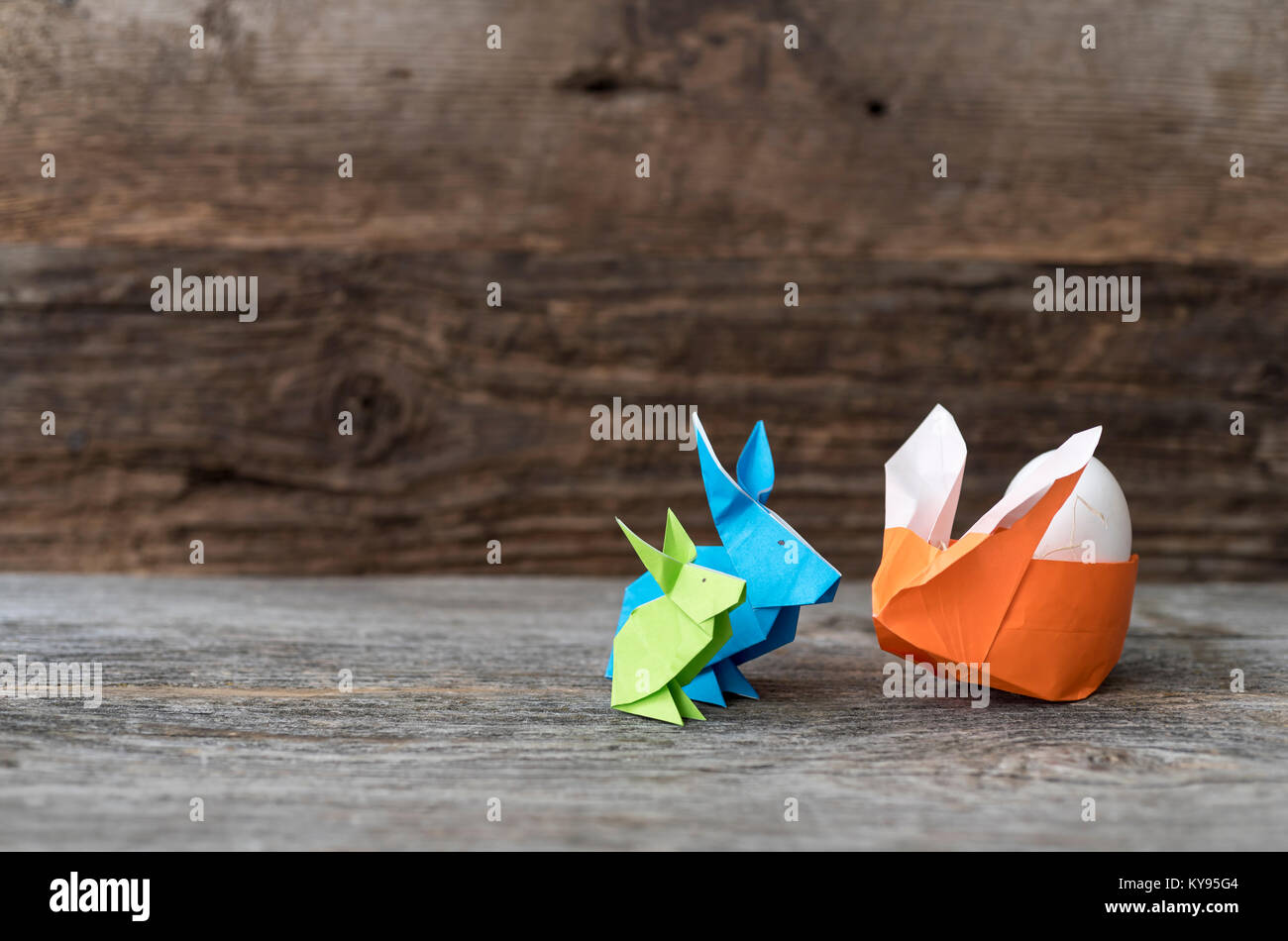 Trois petits lapins de Pâques origami coloré en vert, bleu et orange en papier, un farci de paille, berçant un œuf de Pâques ou de printemps Banque D'Images