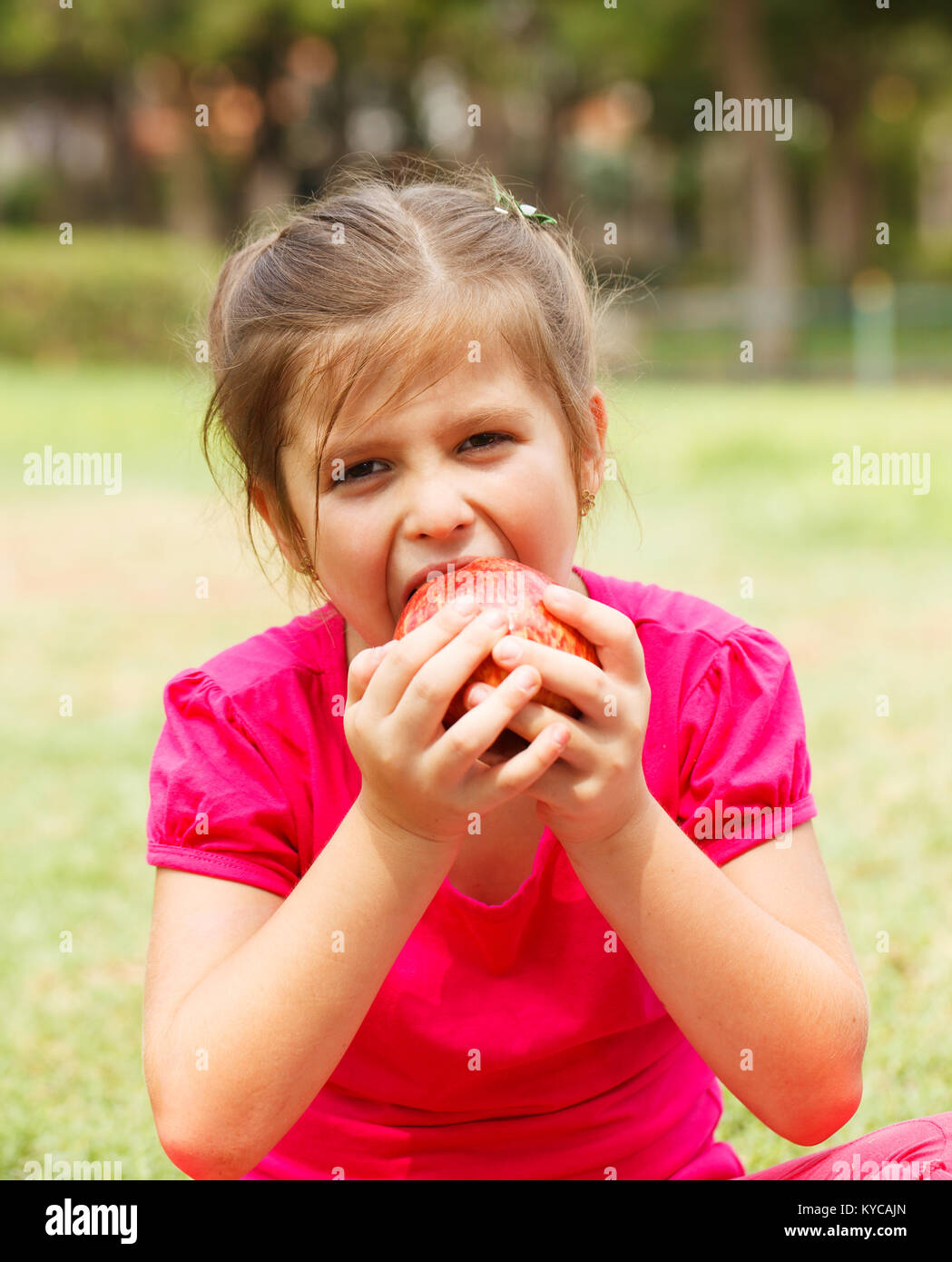 Little Girl eating red apple avec l'expression du visage Banque D'Images