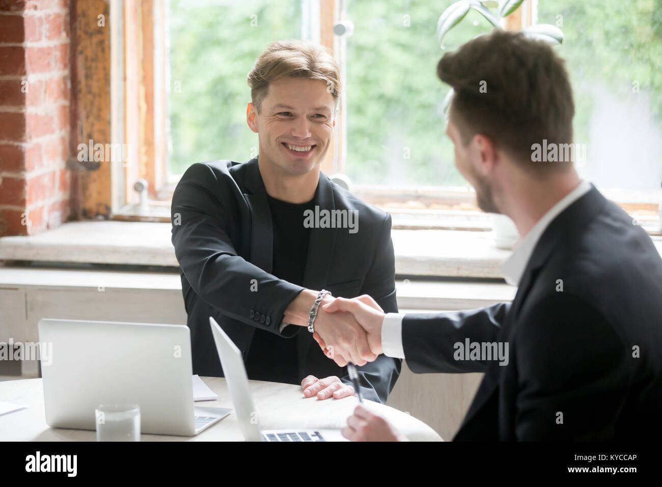 Les entrepreneurs satisfaits se serrer la main après que les négociations sur meeting in office, deux hommes d'affaires prospères en costume assis à 24 faire de bonne affaire, h Banque D'Images