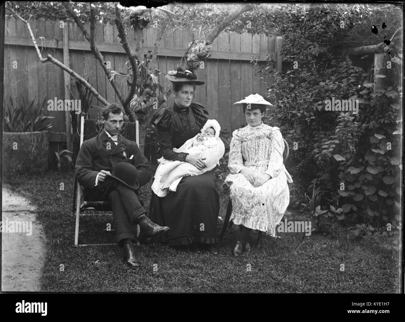 Photographie de trois adultes avec un bébé dans un jardin, capturant un moment domestique calme et illustrant la vie familiale et sociale du début du XXe siècle. Banque D'Images