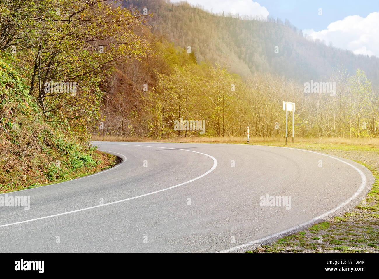 La route tourne à gauche entre les petites montagnes et forêts illuminées par la lumière du soleil. Banque D'Images