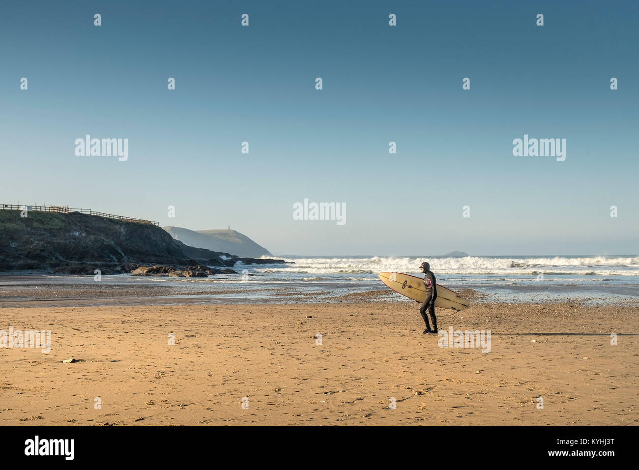 Polzeath - un surfeur marchant sur la plage de Polzeath transportant un surf de la côte nord des Cornouailles. Banque D'Images