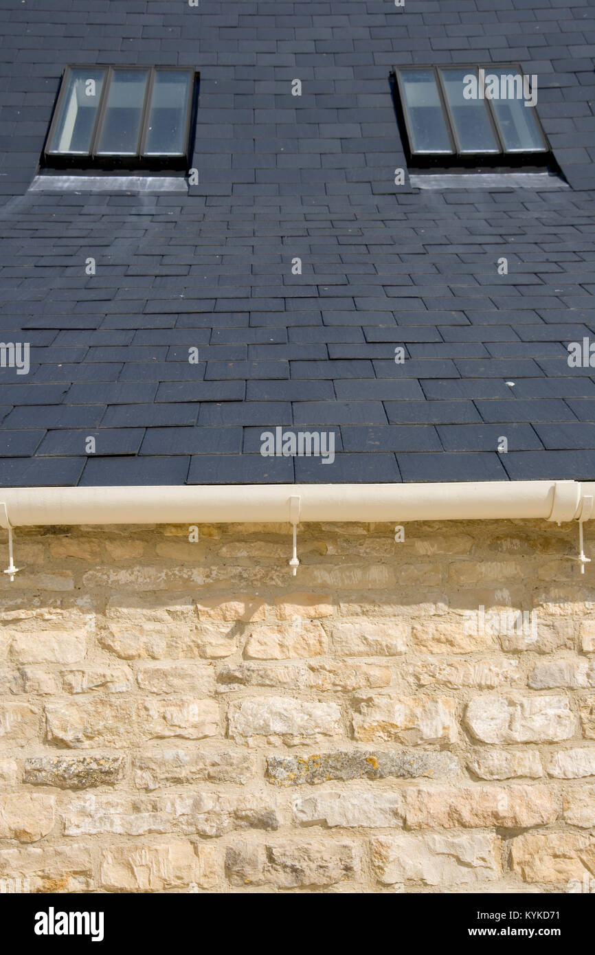 Deux puits de lumière dans un toit de tuiles d'ardoise au-dessus d'un mur en pierre calcaire Banque D'Images