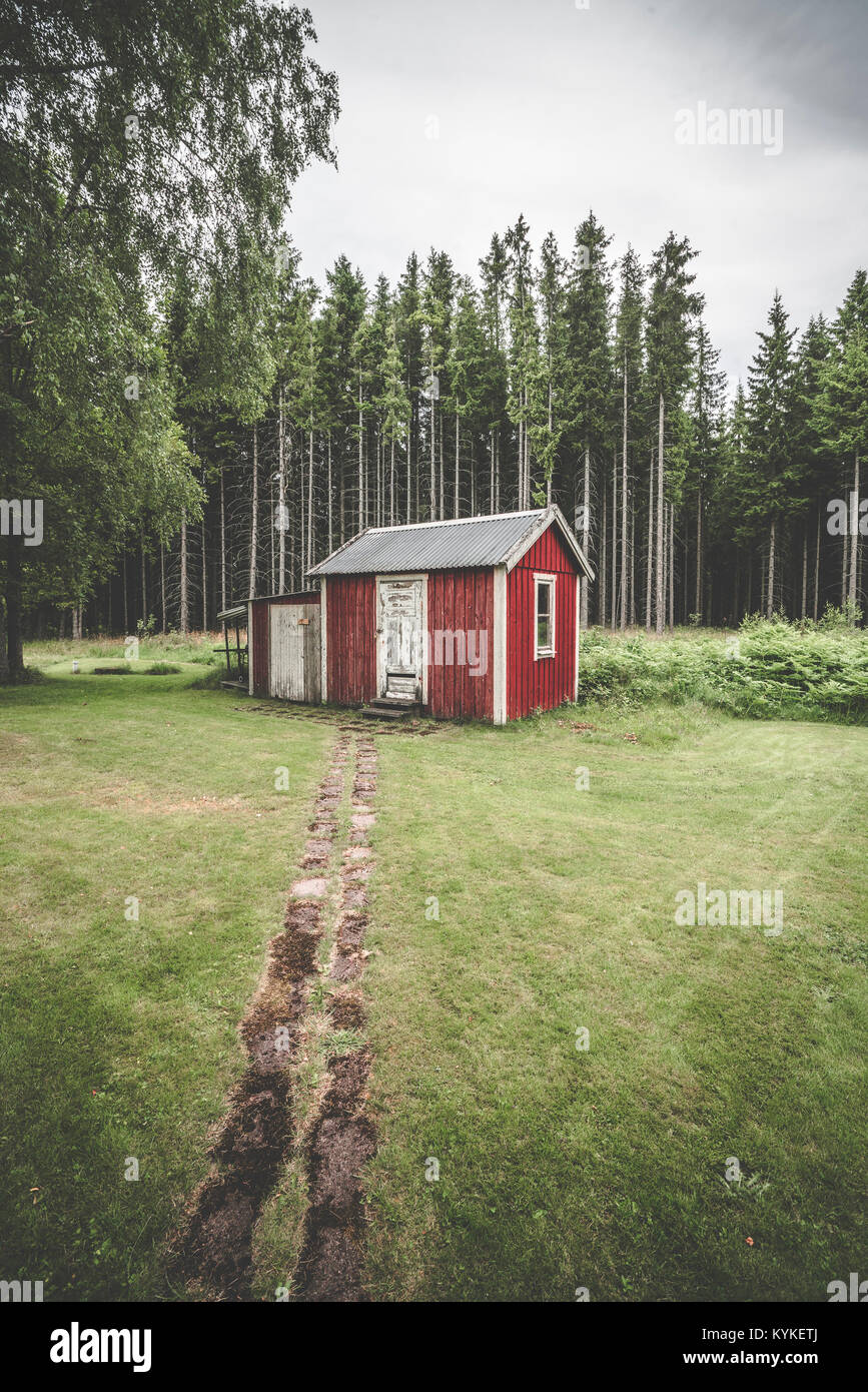 Sentier qui mène jusqu'à un petit chalet dans les bois rouge entourée de grands pins en Suède Banque D'Images