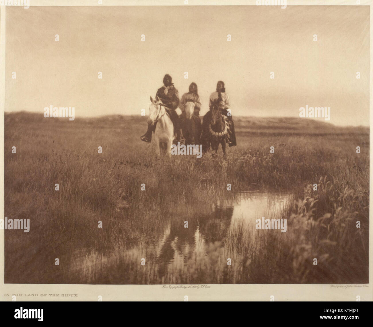 Photographie d'Edward S. Curtis montrant trois Amérindiens à cheval, faisant partie de la nation Sioux, chevauchant les plaines. L'image capture leur tenue traditionnelle et le vaste paysage des prairies. Banque D'Images