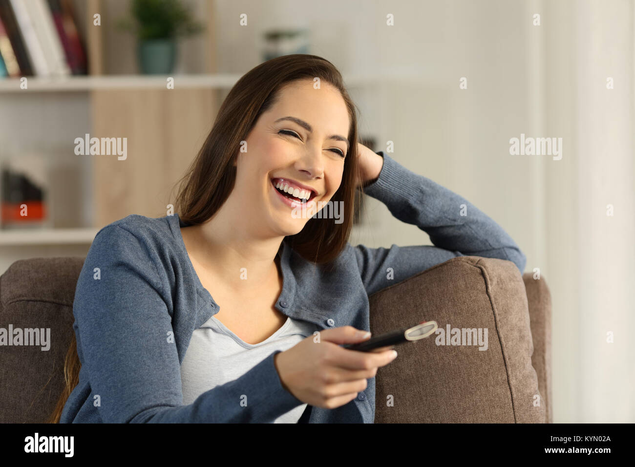 Girl laughing regarder la télévision assis sur un canapé dans la salle de séjour à la maison Banque D'Images