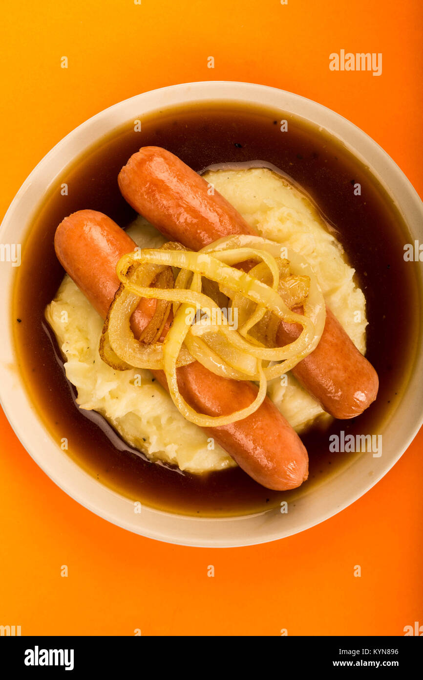 Ou scandinave Norwegian saucisses et purée de pommes de terre avec la sauce et des oignons frits contre une Orange Backgroound Banque D'Images