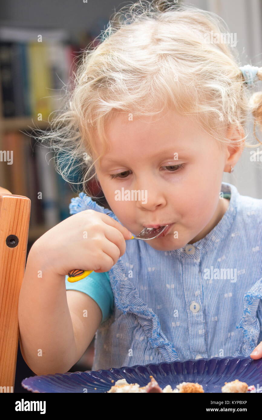 Cute little girl eating dessert sur la plaque avec une fourchette Banque D'Images