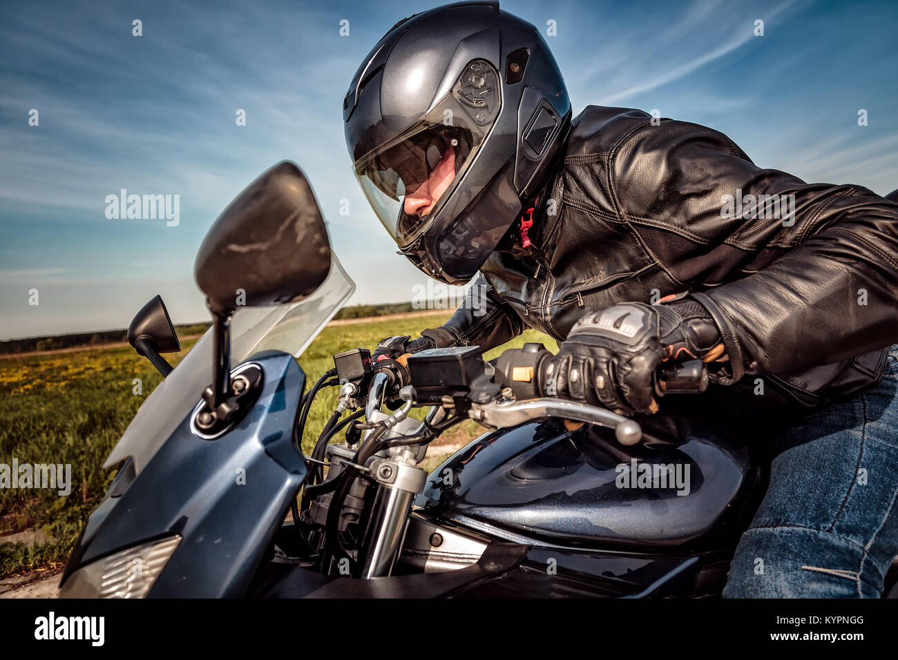 Biker dans casque et blouson de cuir racing sur la route Banque D'Images