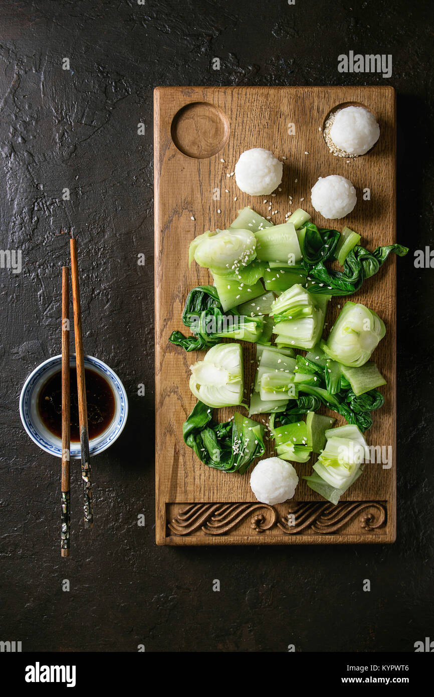 Sauté de bok choy ou chou chinois avec de la sauce soja et de boules de riz servi sur planche à découper en bois décoratif avec des baguettes sur la texture sombre backg Banque D'Images