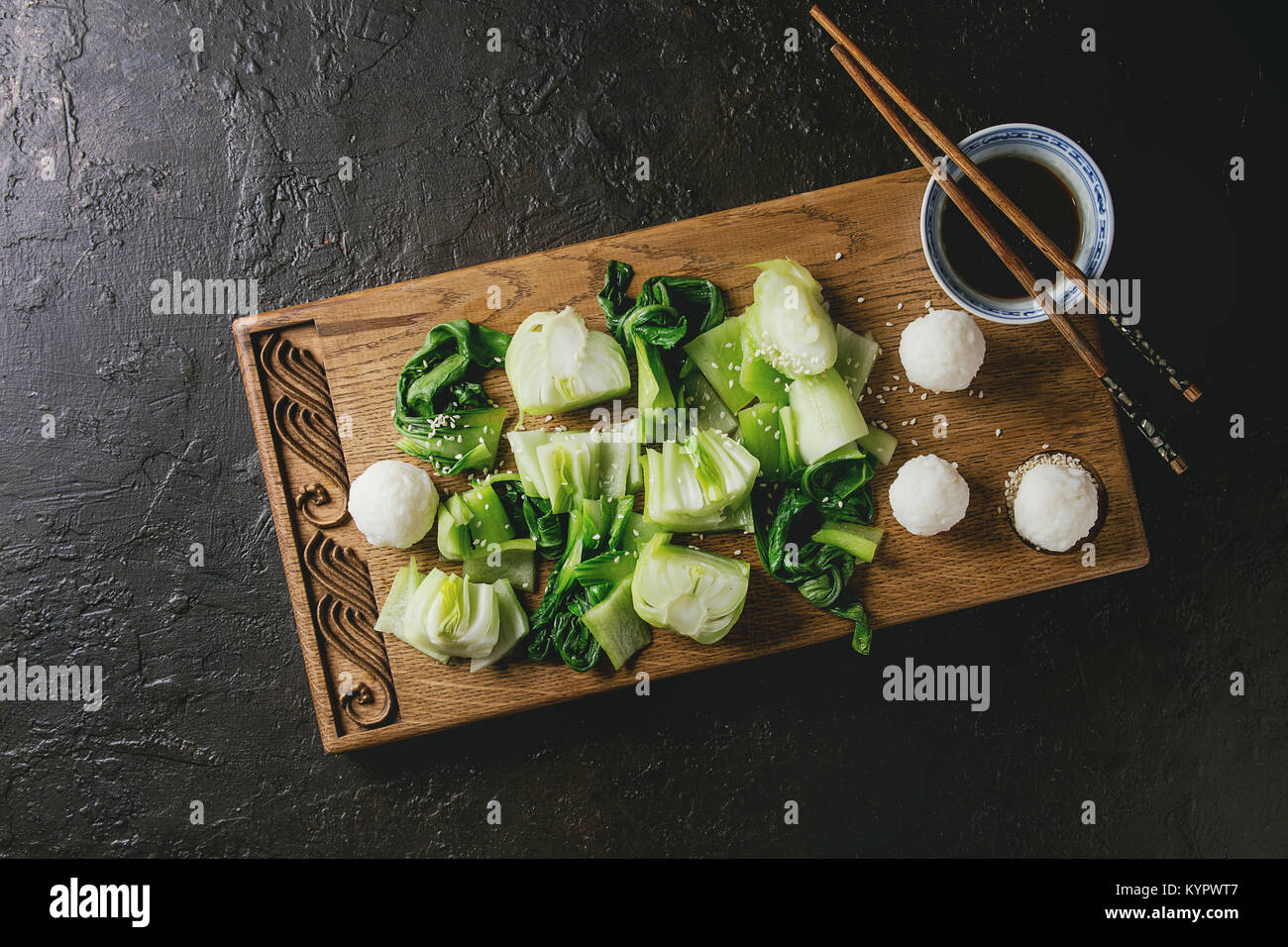 Sauté de bok choy ou chou chinois avec de la sauce soja et de boules de riz servi sur planche à découper en bois décoratif avec des baguettes sur la texture sombre backg Banque D'Images