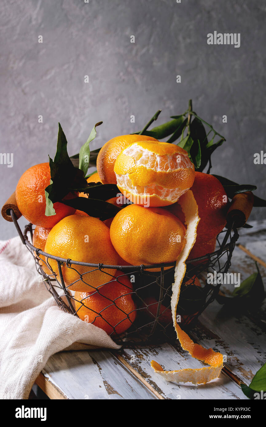 Clémentines ou mandarines biologiques mûrs avec des feuilles dans panier debout avec cuisine serviettes sur la planche en bois blanc table avec mur gris en arrière-plan. Rus Banque D'Images