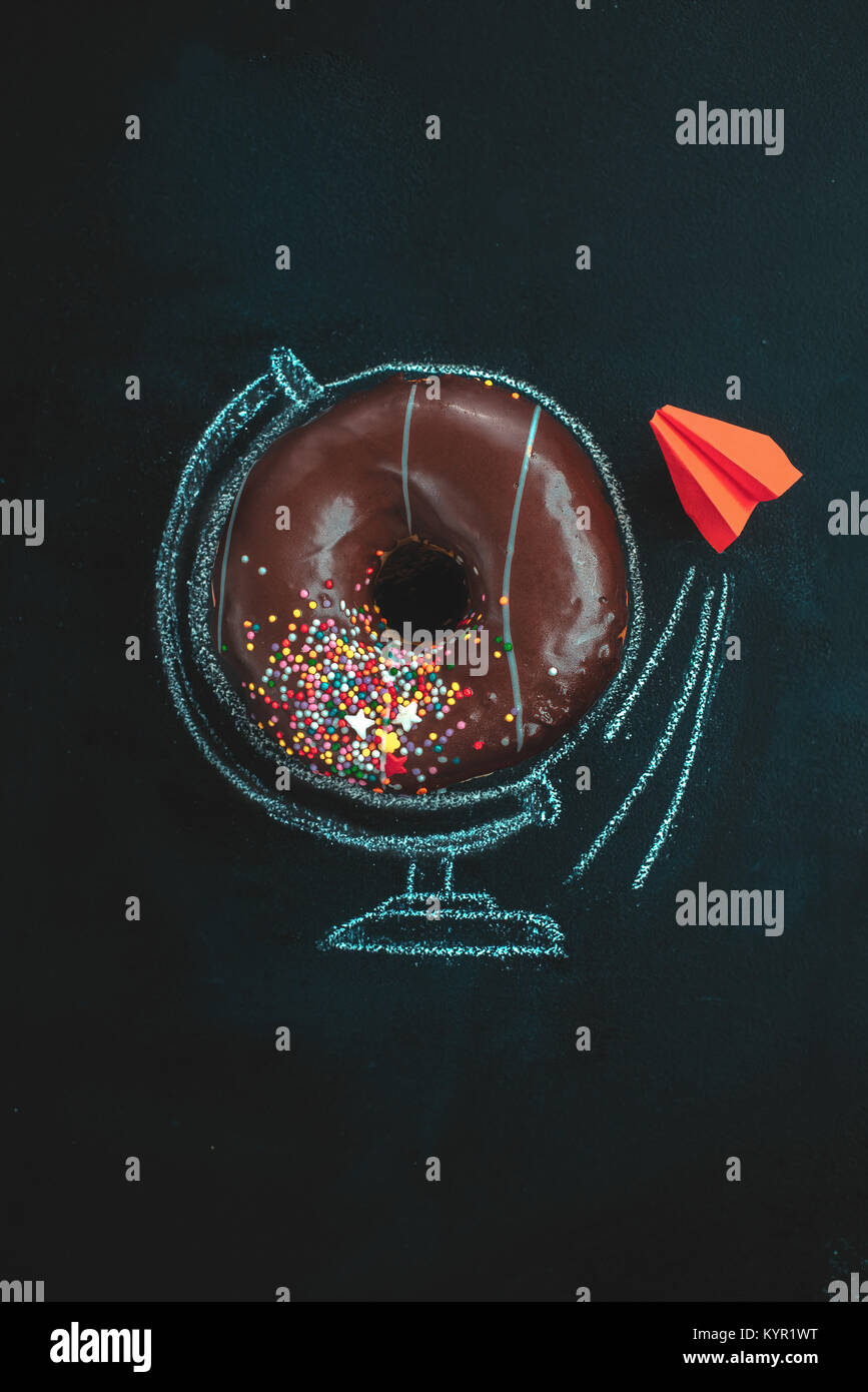Beignet au chocolat avec dessin à la craie d'un globe et un avion origami rouge. Concept créatif. Les aliments à faible clés la photographie. Banque D'Images