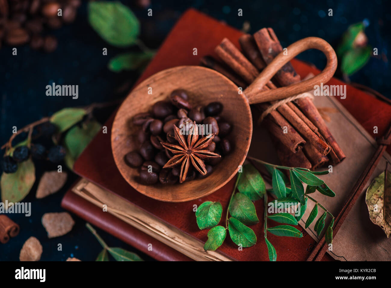 Grains de café dans une main en bois vintage scoop sur un fond sombre avec des étoiles d'anis, la cannelle, le sucre brun et les feuilles. Retro still life with barista Banque D'Images