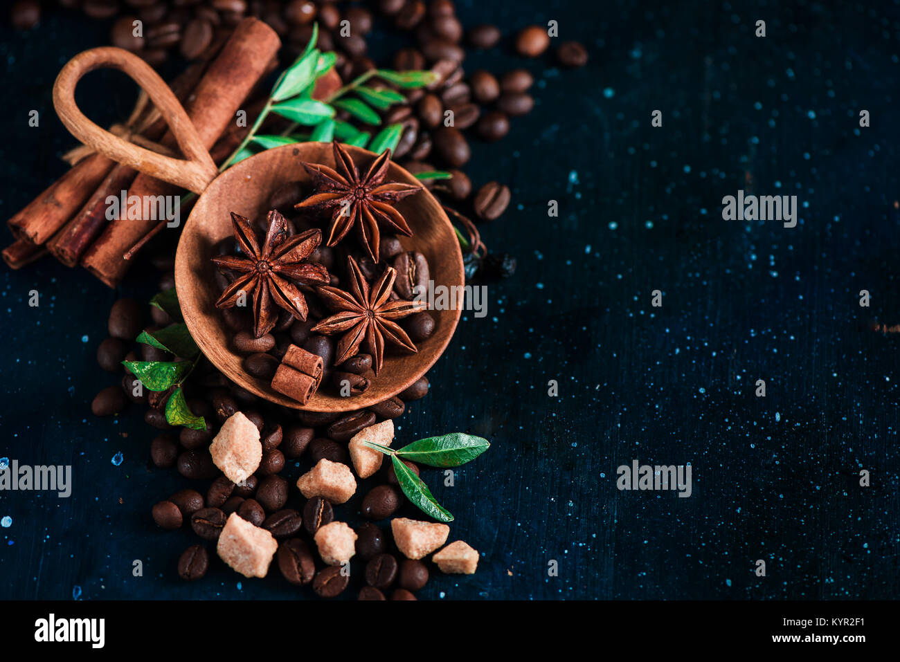 Grains de café dans une main en bois vintage scoop sur un fond sombre avec des étoiles d'anis, la cannelle, le sucre brun et les feuilles. Retro still life with barista Banque D'Images