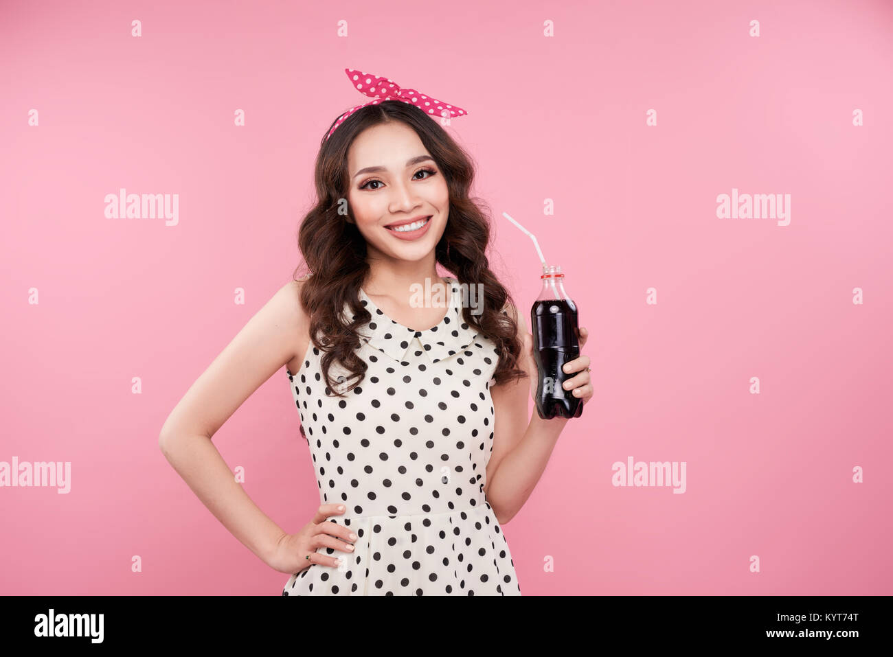 Fashion asian woman holding bouteille de coke, posant contre fond rose Banque D'Images