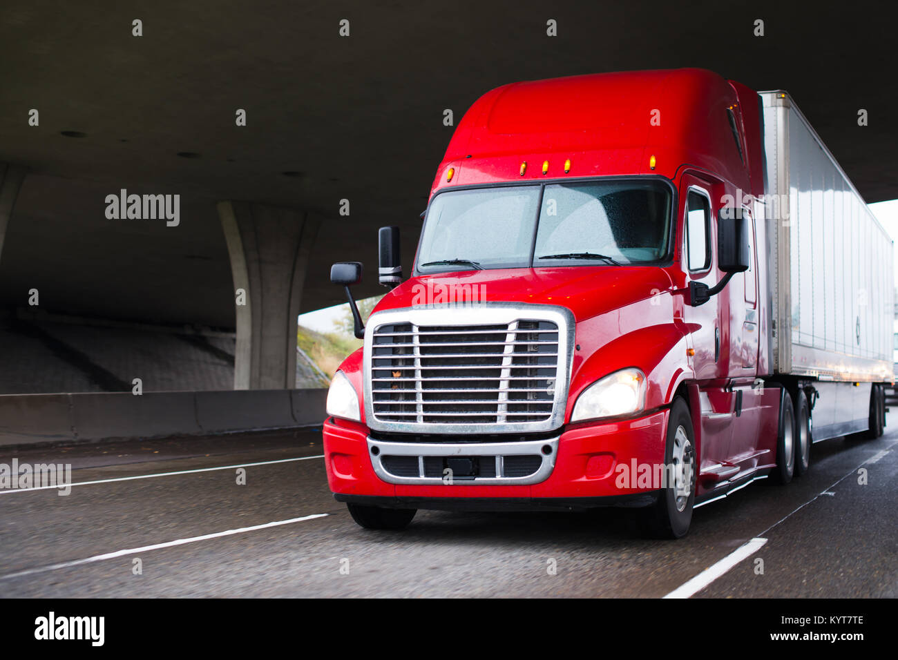 Un gros camion camion semi modernes de transport long avec une grande cabine pour l'amélioration des caractéristiques aérodynamiques se déplace sous le pont sur une route Banque D'Images