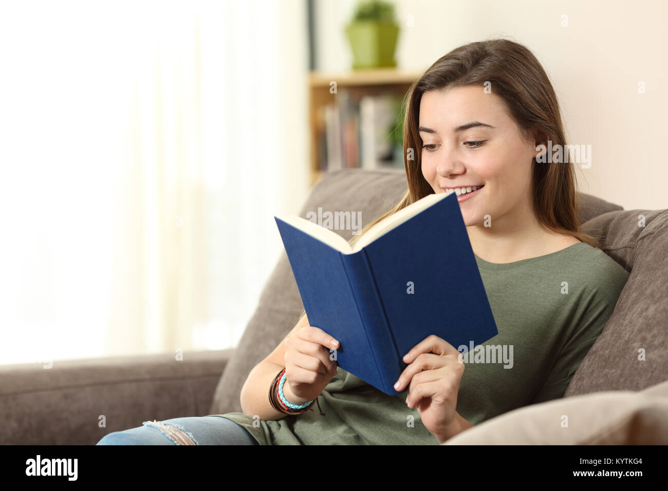 Portrait d'un adolescent heureux de lire un livre sur un canapé dans la salle de séjour à la maison Banque D'Images