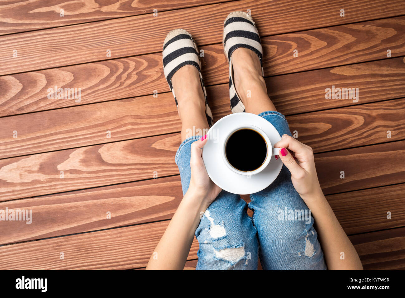 Femme de boire du café tout en étant assis sur un plancher en bois. Vue d'en haut Banque D'Images