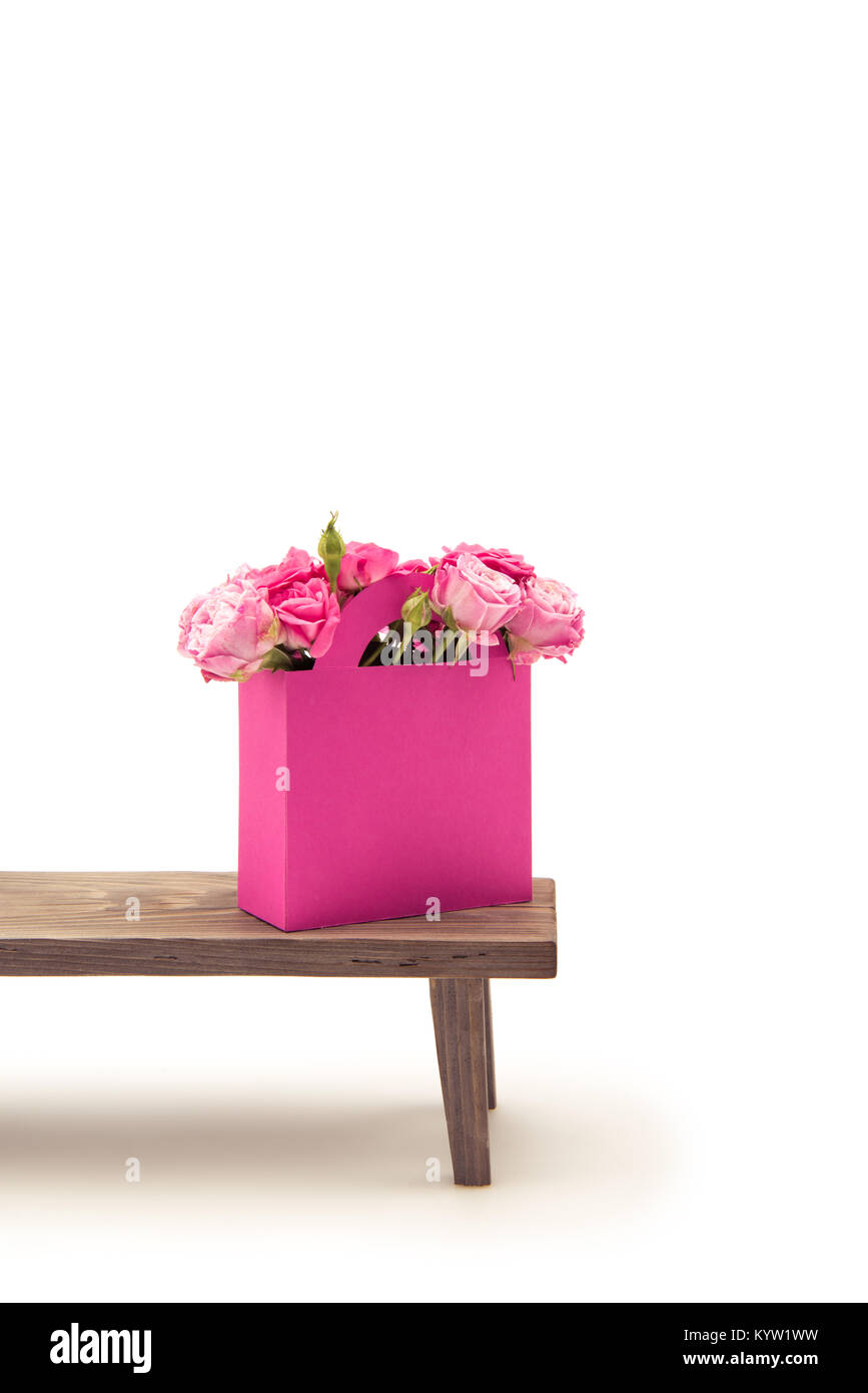 Vue rapprochée de la floraison des fleurs rose tendre en rose sac de papier sur banc en bois isolé sur blanc Banque D'Images