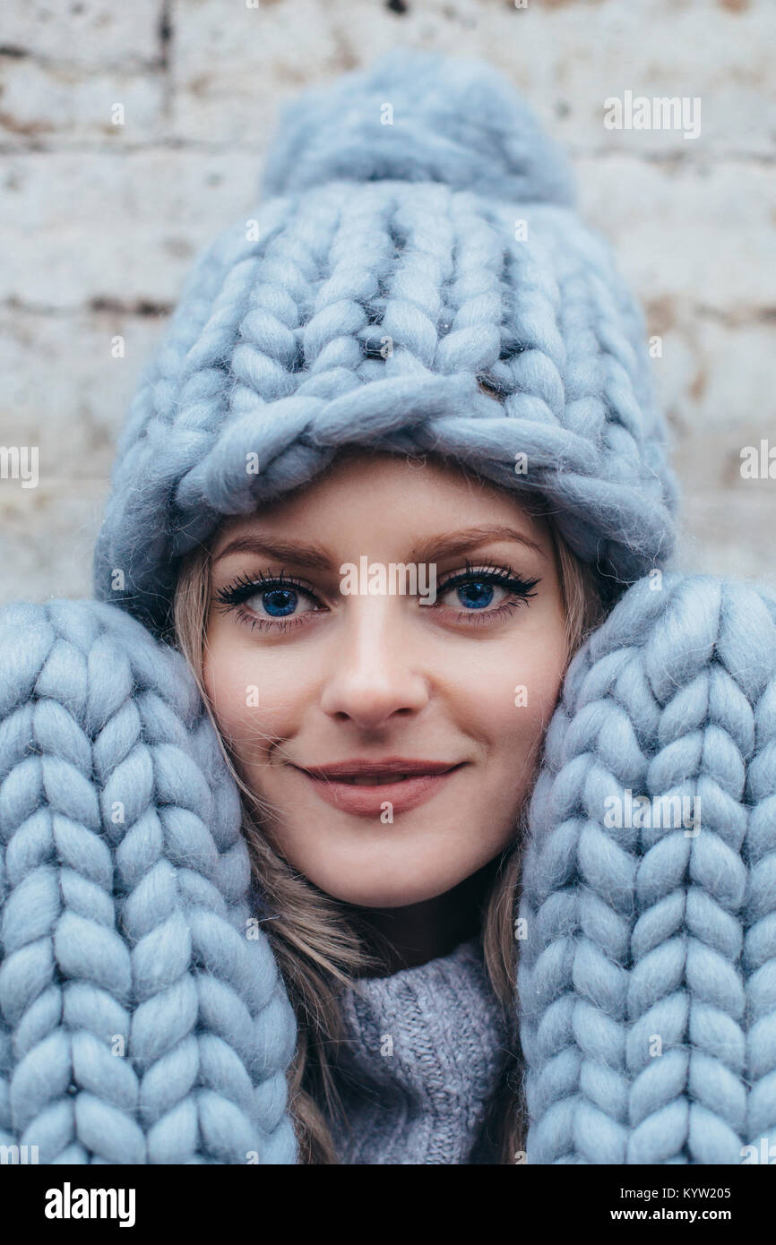 Jeune femme blonde de smoky blue hat tricoté des mitaines tricotées, et blue-jeans faire posant avec un mur gris pierre sur l'arrière-plan Banque D'Images