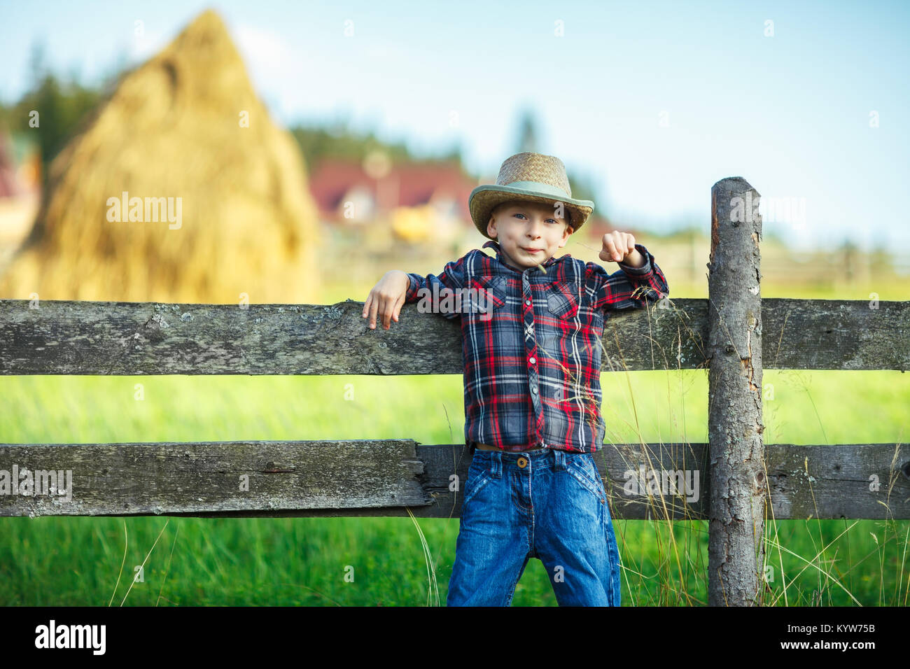 Garçon appuya son dos sur clôture en bois, et souriant. Portrait plein air de près. Petit cowboy en posant sur la ferme de l'arrière-plan flou, larg Banque D'Images