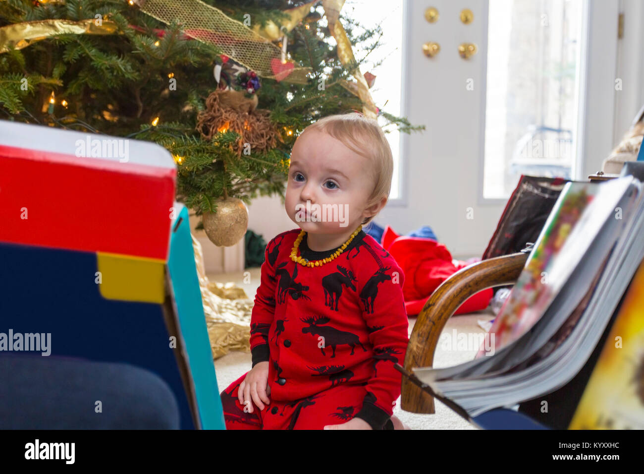 Triste 1 ans enfant en pyjama rouge assis sur le plancher à côté de l'arbre de Noël Banque D'Images