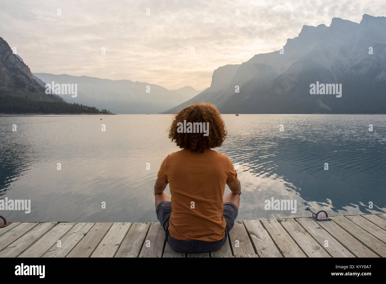 De randonneur while sitting on jetty sur le lac Minnewanka contre montagne Banque D'Images